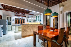 A spacious kitchen with modern appliances, a central island, and a dining area with a wooden table and wicker chairs.