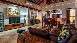 A spacious living area with a large flat-screen TV, comfortable seating, and a kitchen in the background. - Villa Livo (Denpasar)