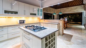 A modern kitchen with white cabinets, a granite countertop, a built-in gas stove, and a microwave. - Villa Livo (Denpasar)