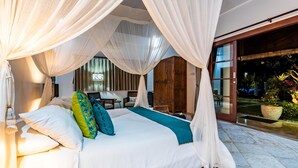 A spacious bedroom with a large bed, white bedding, and a canopy. There is a wooden wardrobe and a small table with chairs. - Villa Livo (Denpasar)