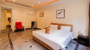 Une chambre d’hôtel avec un grand lit, un fauteuil rouge, un bureau et une œuvre d’art accrochée au mur.
