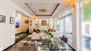 Un hall d’hôtel moderne avec une table à manger en verre, des sièges confortables et de grandes fenêtres offrant une vue panoramique.