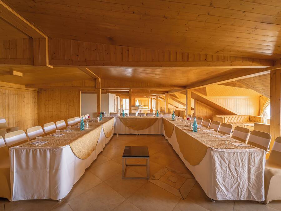 Une grande salle de conférence au plafond haut et aux murs en bois, équipée d’une longue table et de chaises, ainsi que d’une petite table placée au centre.