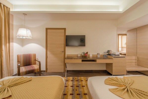 Habitación de hotel con dos camas, un escritorio, un televisor de pantalla plana, una silla y una mesita de noche con artículos de aseo.