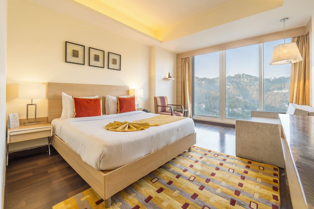 Ein Hotelzimmer mit einem großen Bett, einem Schreibtisch, einem Stuhl und Blick auf die Stadt.