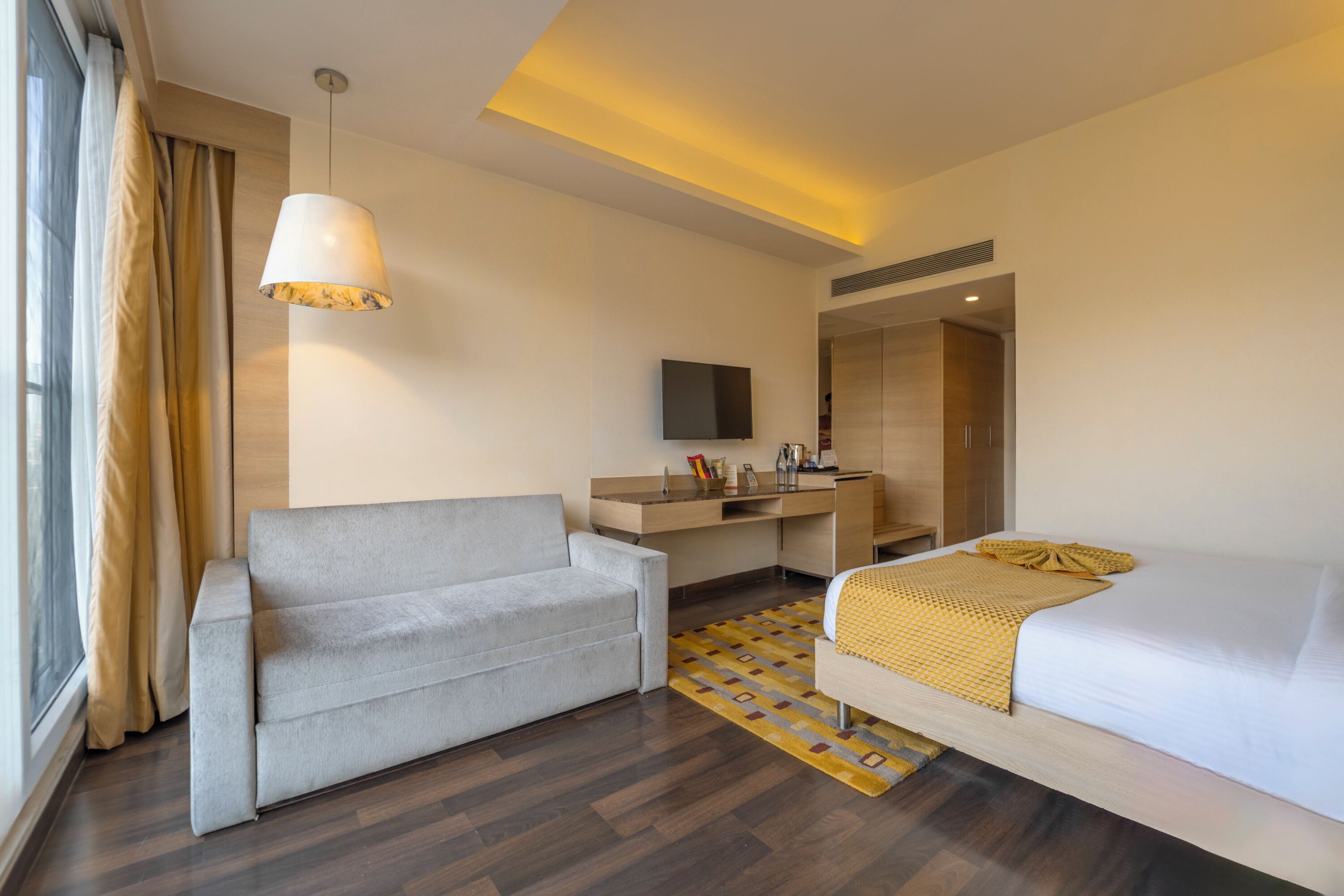 A modern hotel room with a sofa, a bed, a desk, and a television.