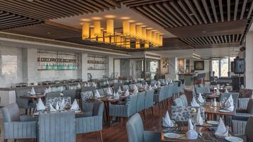A modern restaurant with a long dining area, wooden ceiling, and a bar with shelves of bottles.