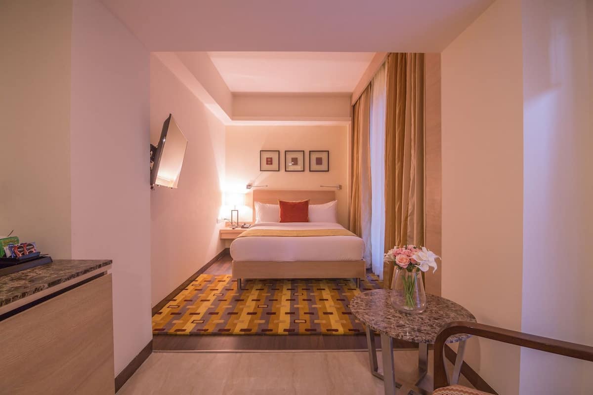 Ein Hotelzimmer mit Bett, Nachttisch, Lampe und einem kleinen Tisch mit Blumenvase.