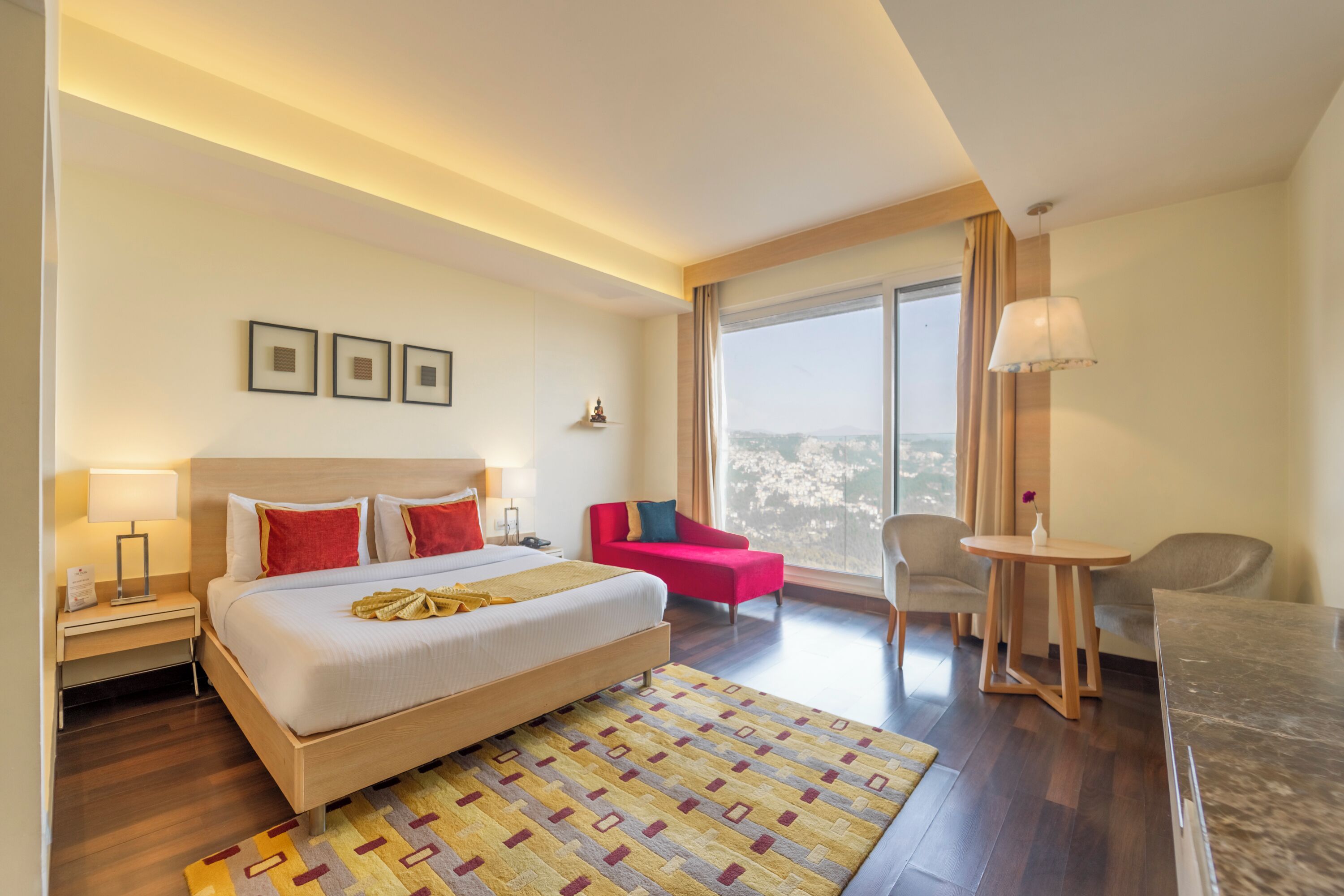 Quarto de hotel com uma cama grande, uma escrivaninha, uma cadeira, uma mesa pequena e vista para a cidade.