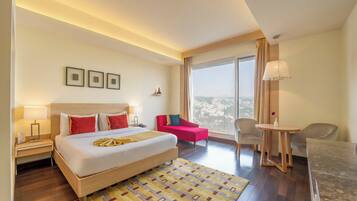 Quarto de hotel com uma cama grande, uma escrivaninha, uma cadeira, uma mesa pequena e vista para a cidade.