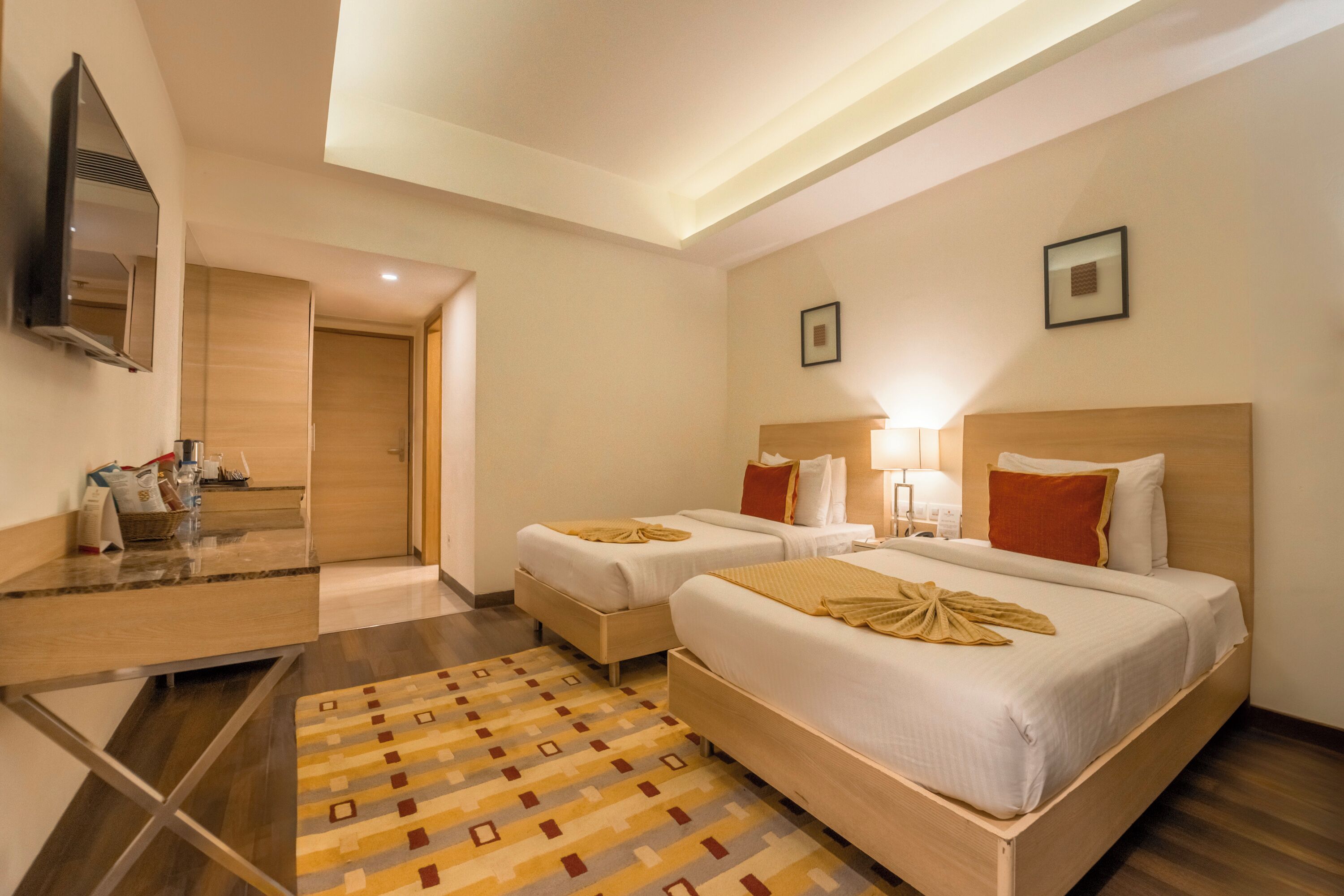 A hotel room with two beds, a TV, a desk, and a patterned rug.