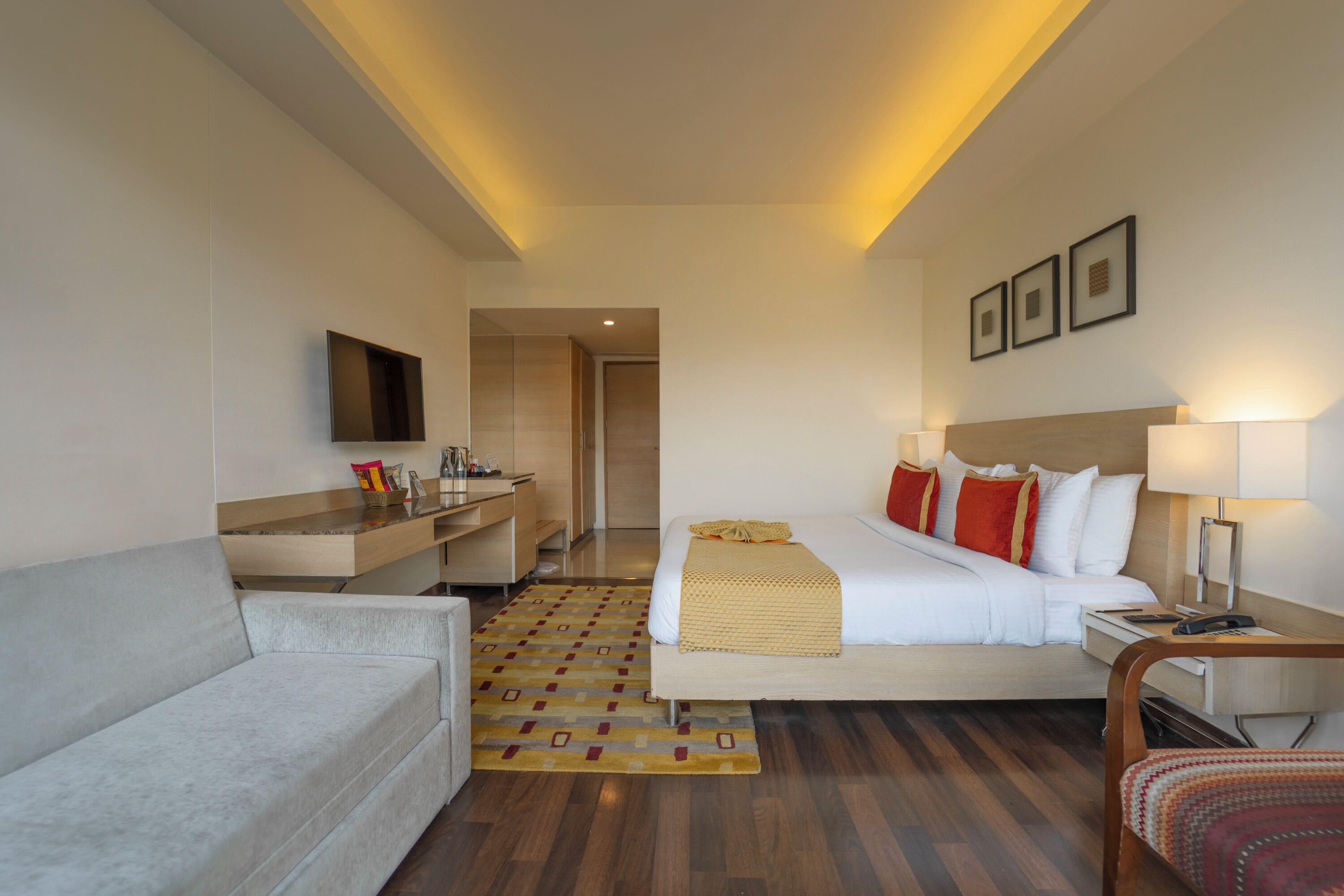 A hotel room with a bed, a sofa, a desk, and a TV.