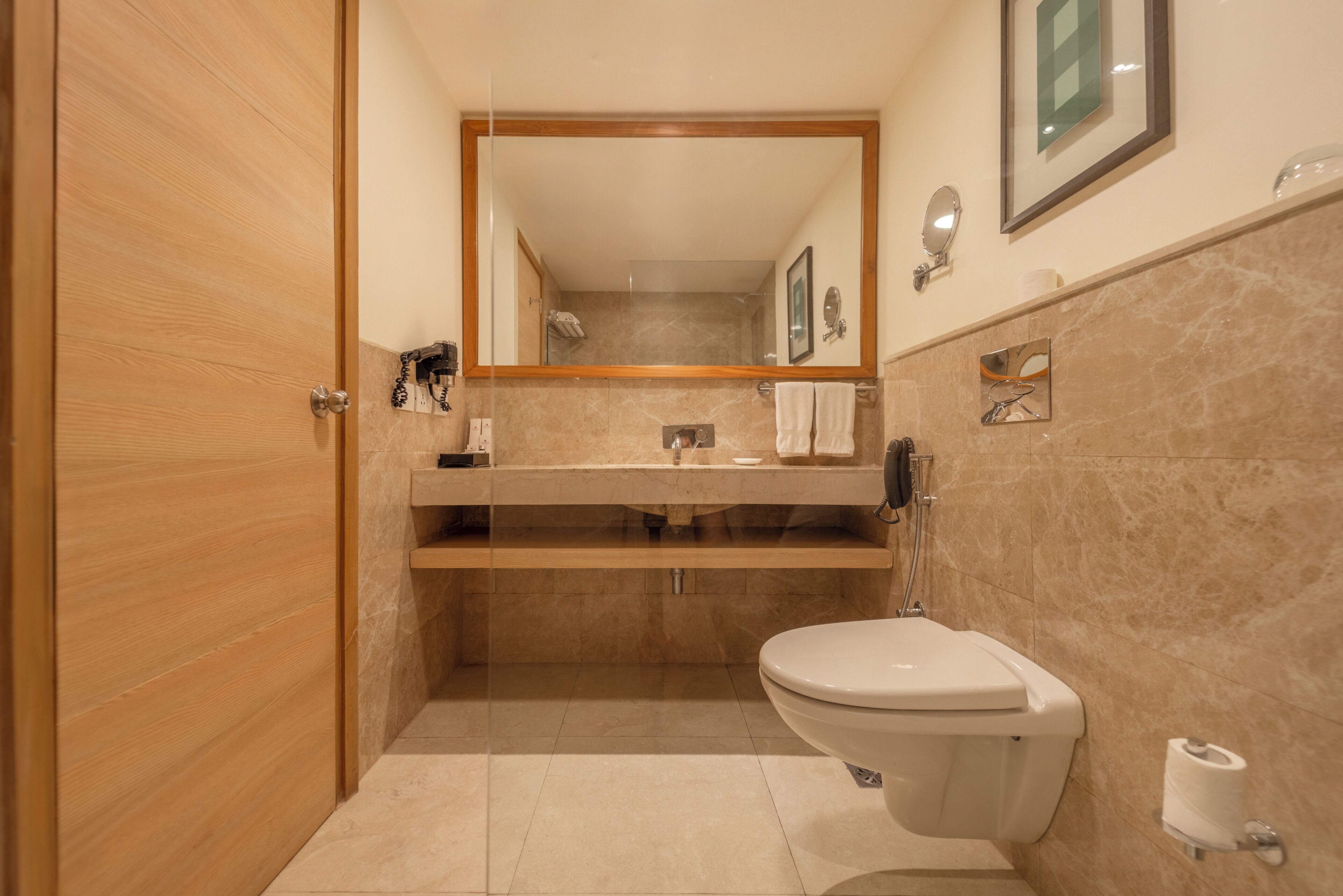 A bathroom with a wooden door, a toilet, a sink with a mirror above it, and a towel rack.
