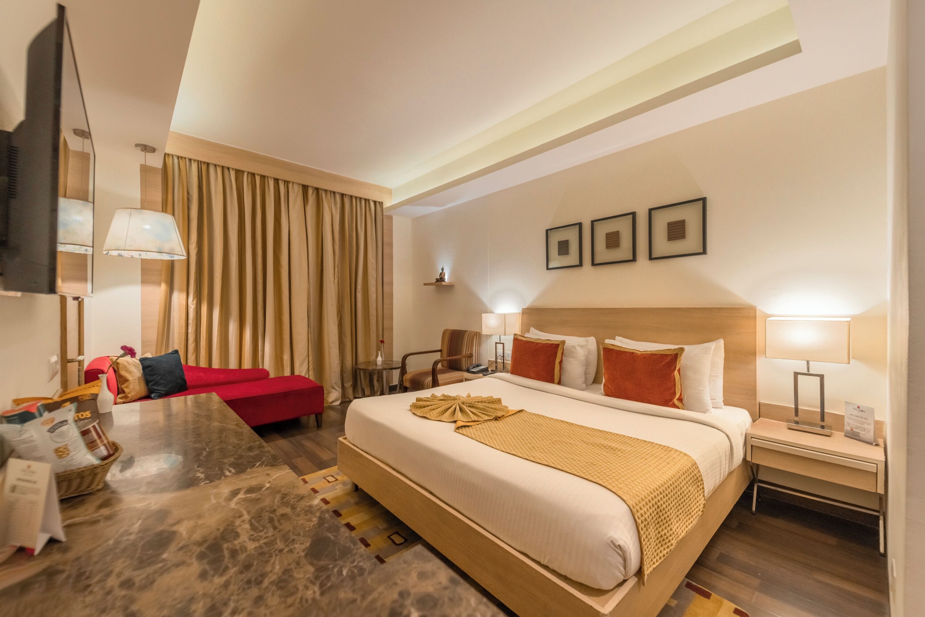A hotel room with a large bed, a red sofa, a dining table, and a TV.
