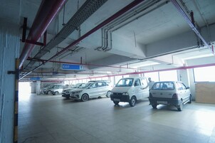 Egy parkolóház, amelyben több autó parkol, egy kijelző tábla és a mennyezeten jól látható csövek találhatók.