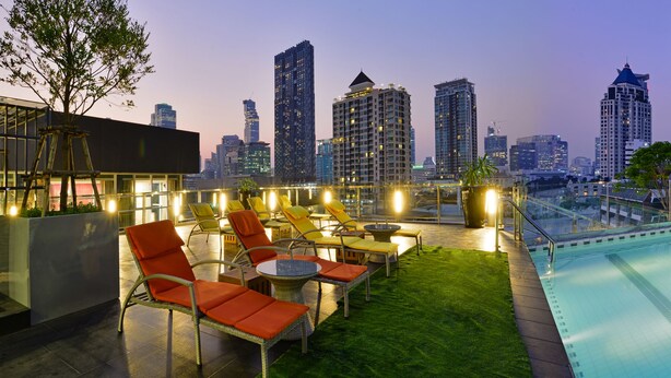 Área de piscina no terraço com vista para o horizonte da cidade ao entardecer.