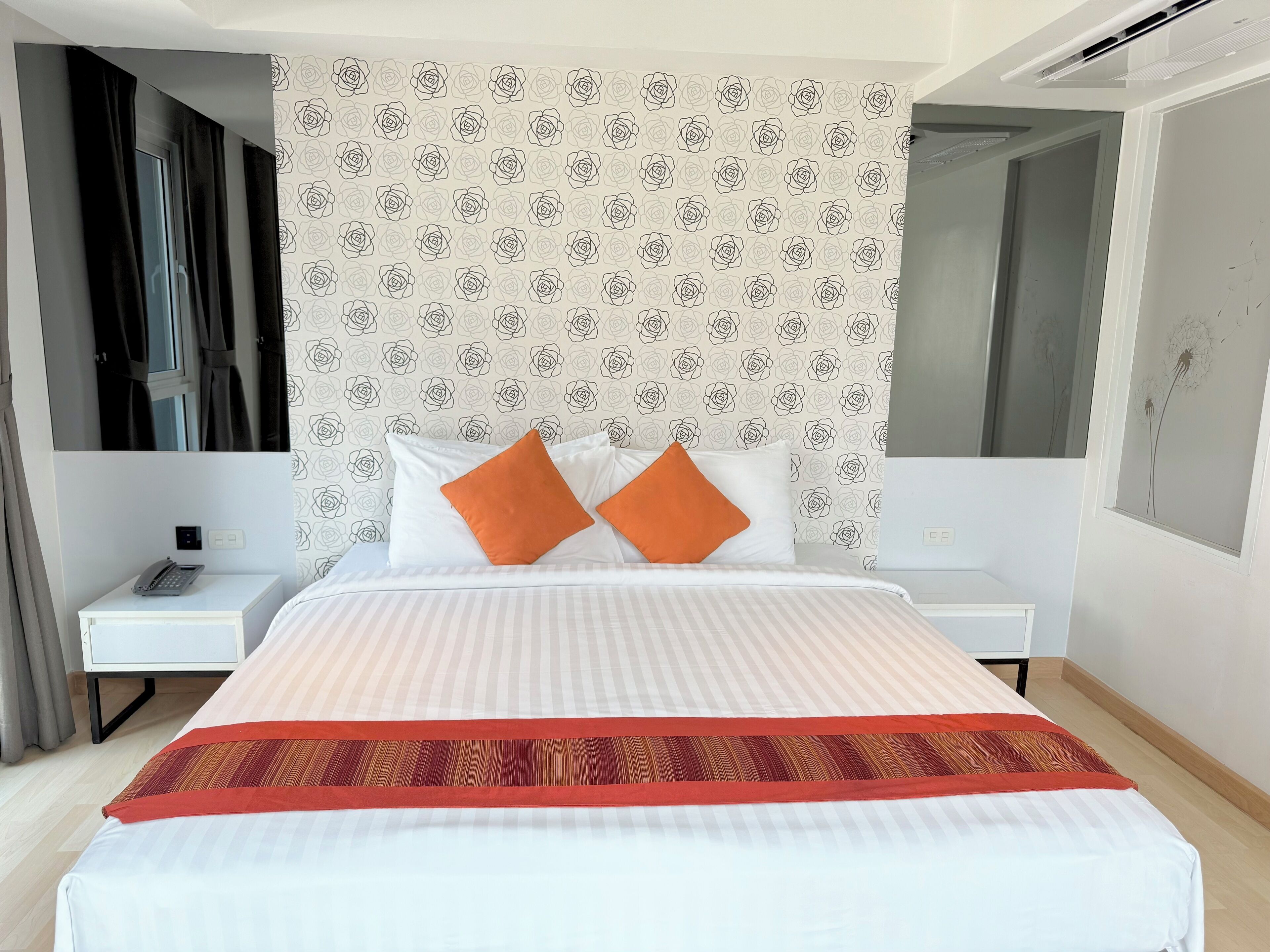 A hotel room with a bed, white nightstands, a telephone, and a wall with a rose pattern.