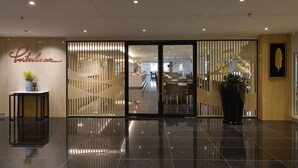 Um hall de hotel moderno com piso lustroso, balcão de recepção e uma grande planta em vaso.