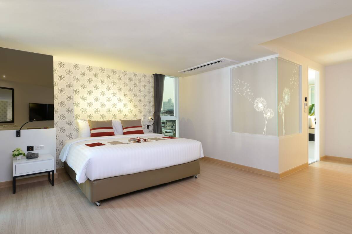 Una camera d'albergo moderna con un letto grande, un comodino con una lampada, una piccola pianta e vista sulla città dalla finestra.