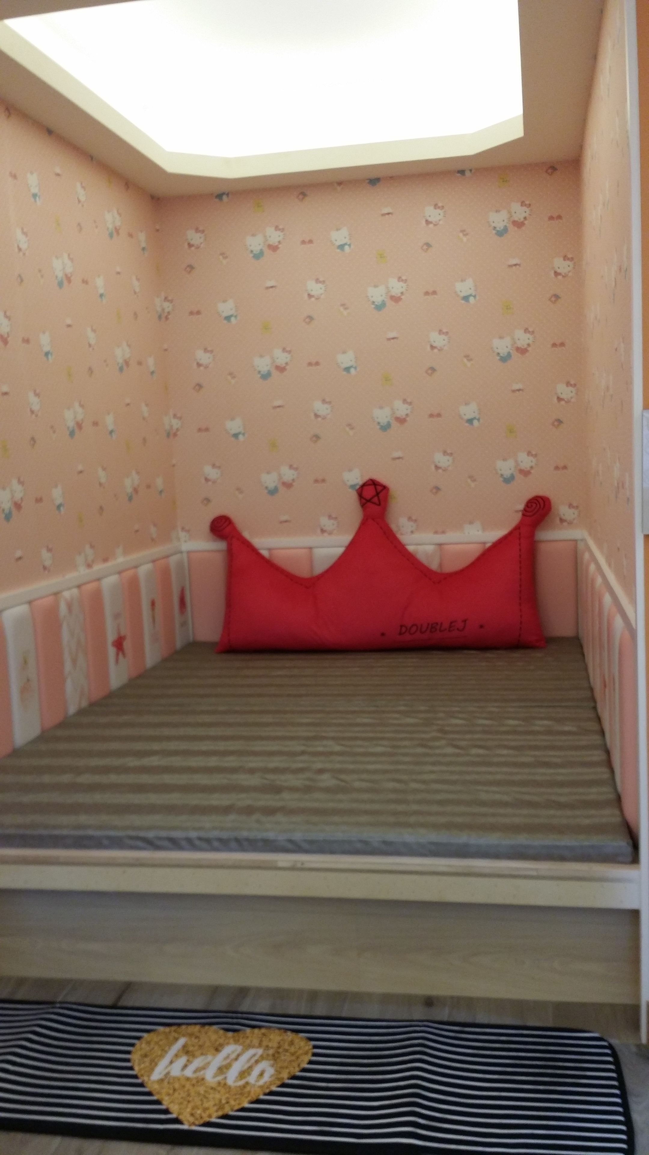Una habitación pequeña y acogedora con una cama, un almohadón rojo y una pared decorada con temática de Hello Kitty.