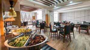 Un vaste espace dédié à la restauration, avec de nombreuses tables et chaises, un buffet proposant une variété de plats, et un design moderne au niveau du plafond.