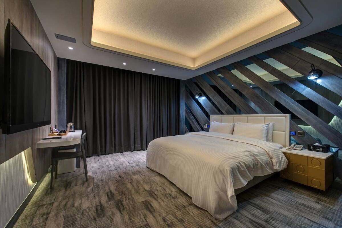 A modern bedroom with a large bed, a desk, and a TV.