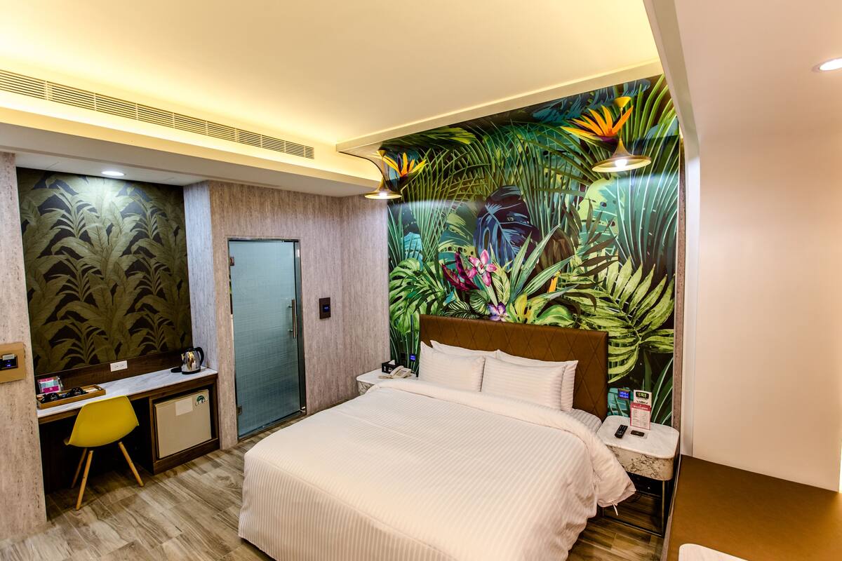 A hotel room with a bed, desk, chair, and a tropical-themed mural.
