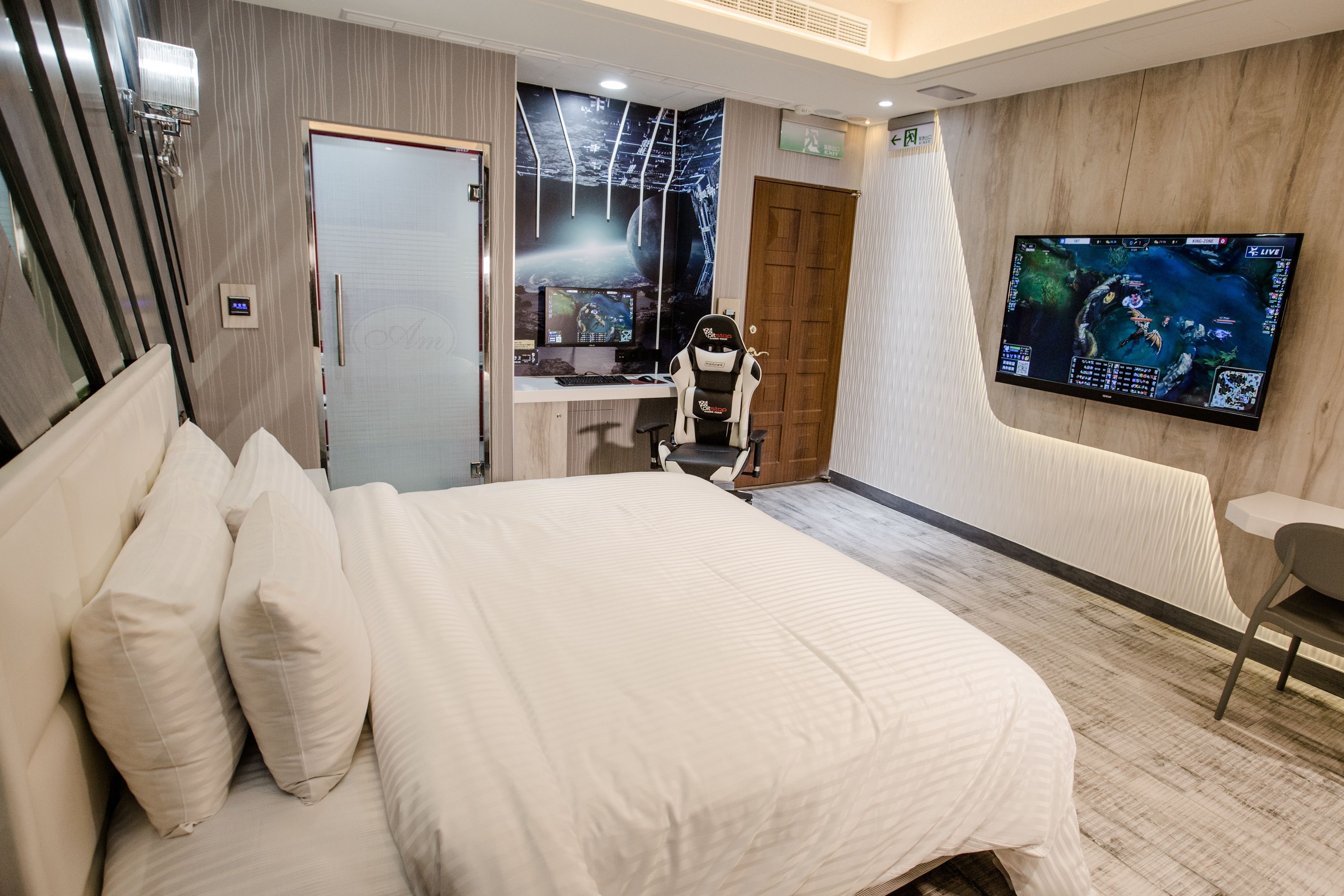 A modern hotel room with a large bed, a desk with a computer, a TV mounted on the wall, and a wooden door.