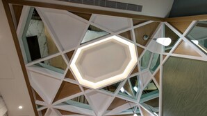 Un intérieur moderne avec un plafond au design géométrique, un éclairage encastré et un luminaire central de forme hexagonale.