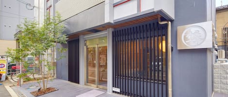 A modern building with a glass entrance, a small tree, and a metal gate.