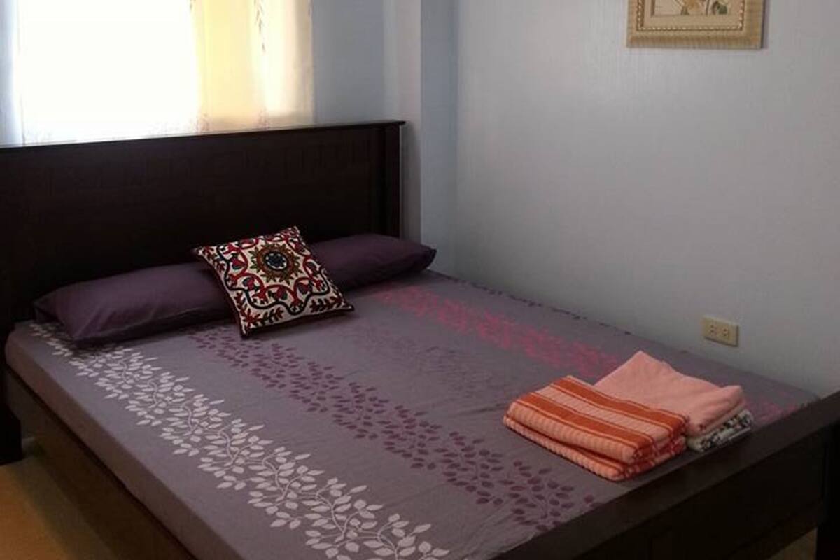 A bedroom with a bed, a window with curtains, a wall-mounted light fixture, and a framed picture.