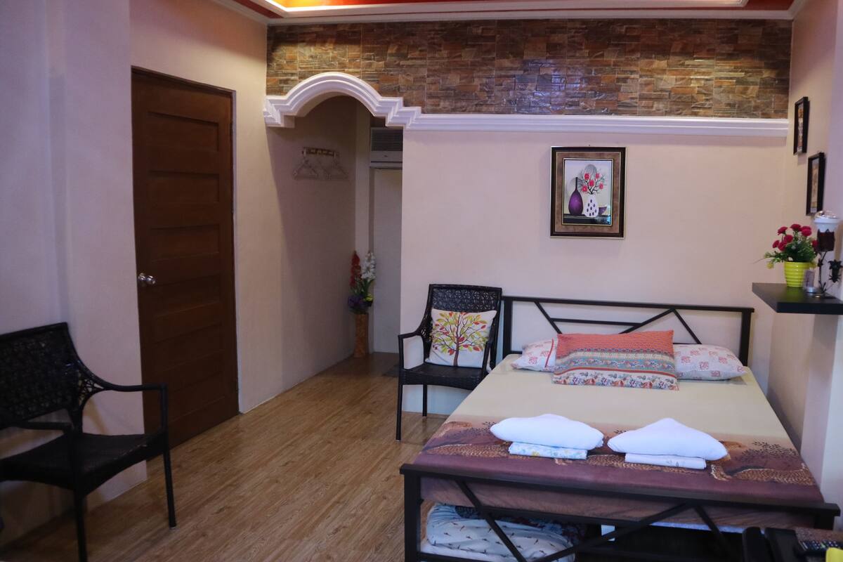 A bedroom with a bed, a chair, a wooden floor, a door, and a wall with a picture.