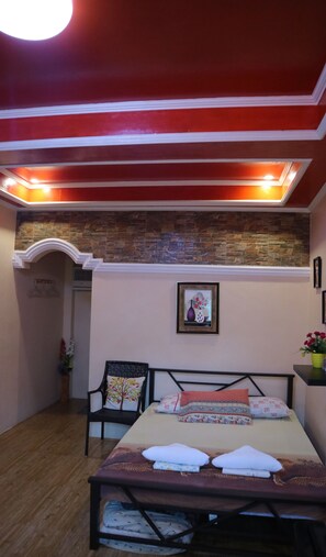 Quarto com cama, cadeira, quadro na parede e luminária no teto.