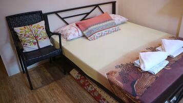 A neatly made bed with patterned bedding, a chair with a decorative pillow, and a wooden floor.