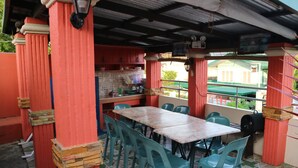 A covered outdoor dining area with a table and chairs, a kitchen area with red cabinets, and a view of a building through the window. - V.Hauschild Transient House B (Alaminos)