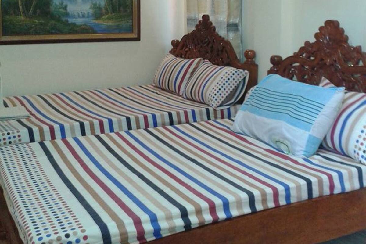 A bedroom with a wooden bed, striped bedding, a stone wall, a painting, and an air conditioning unit.
