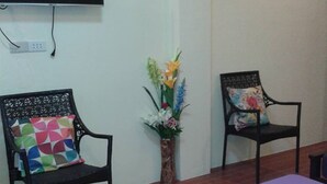 A room with a purple bed, two black chairs with colorful cushions, a vase with flowers, and a flat-screen TV mounted on the wall. - V.Hauschild Transient House B (Alaminos)