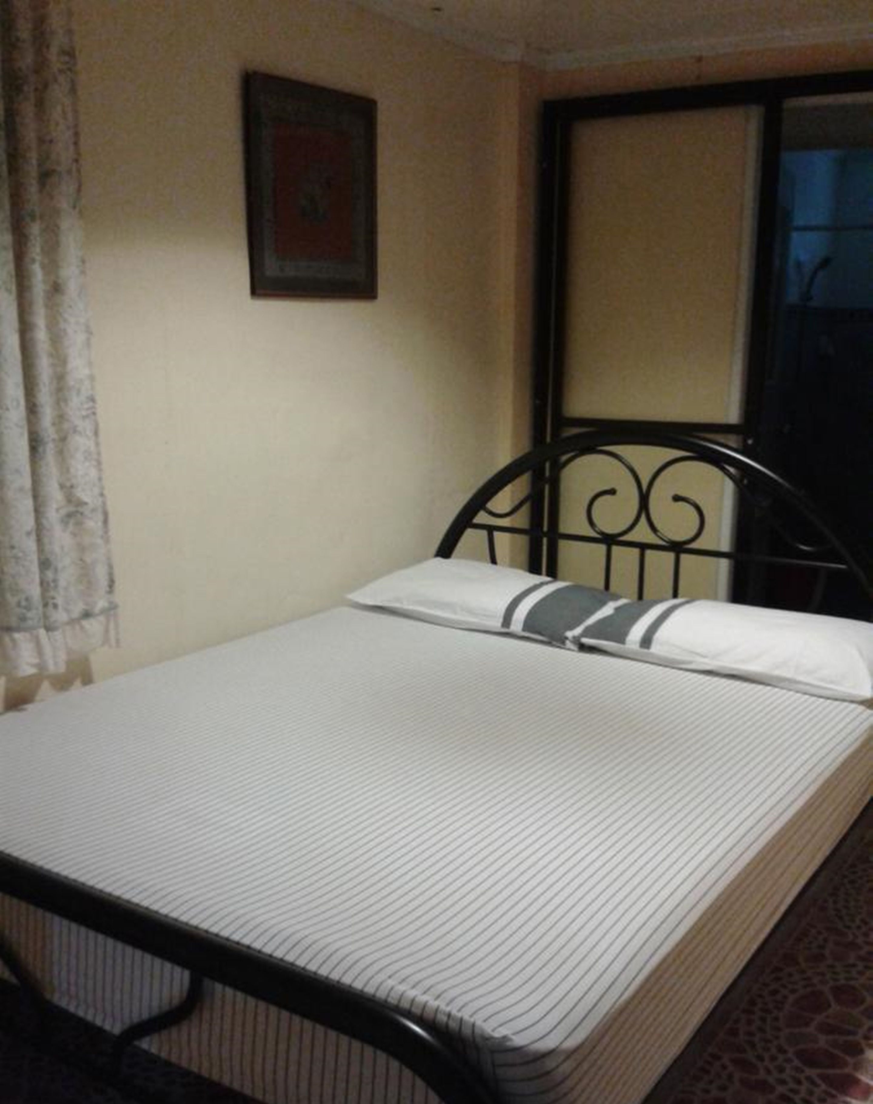 A single bed with a metal frame, a plain mattress, and a pillow with a striped pillowcase.