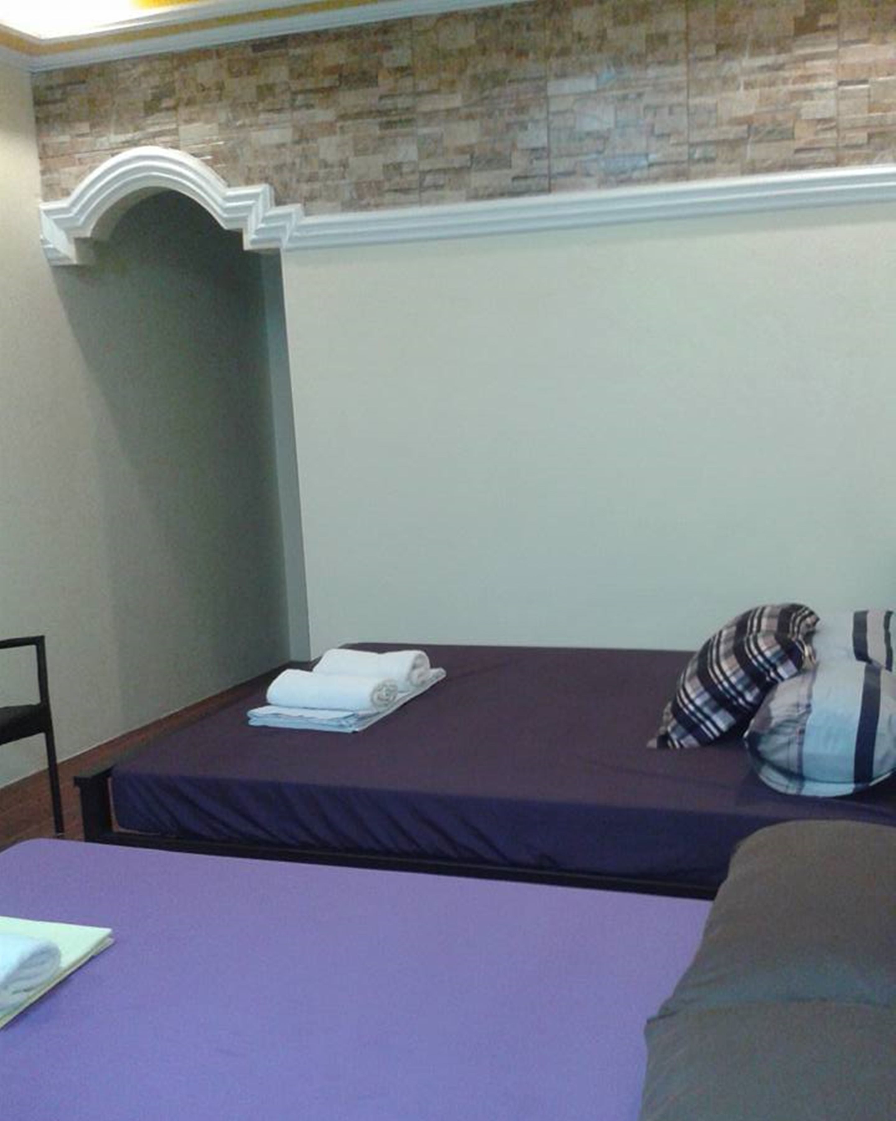 A small, single-bed room with a purple bedspread, a white towel, and a striped pillow.