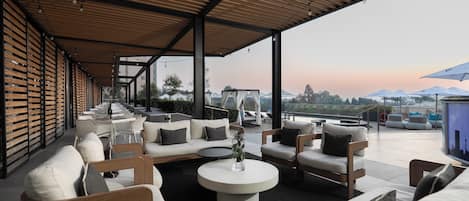 An outdoor seating area with sofas and tables, a view of the mountains, and a covered section with wooden slats.