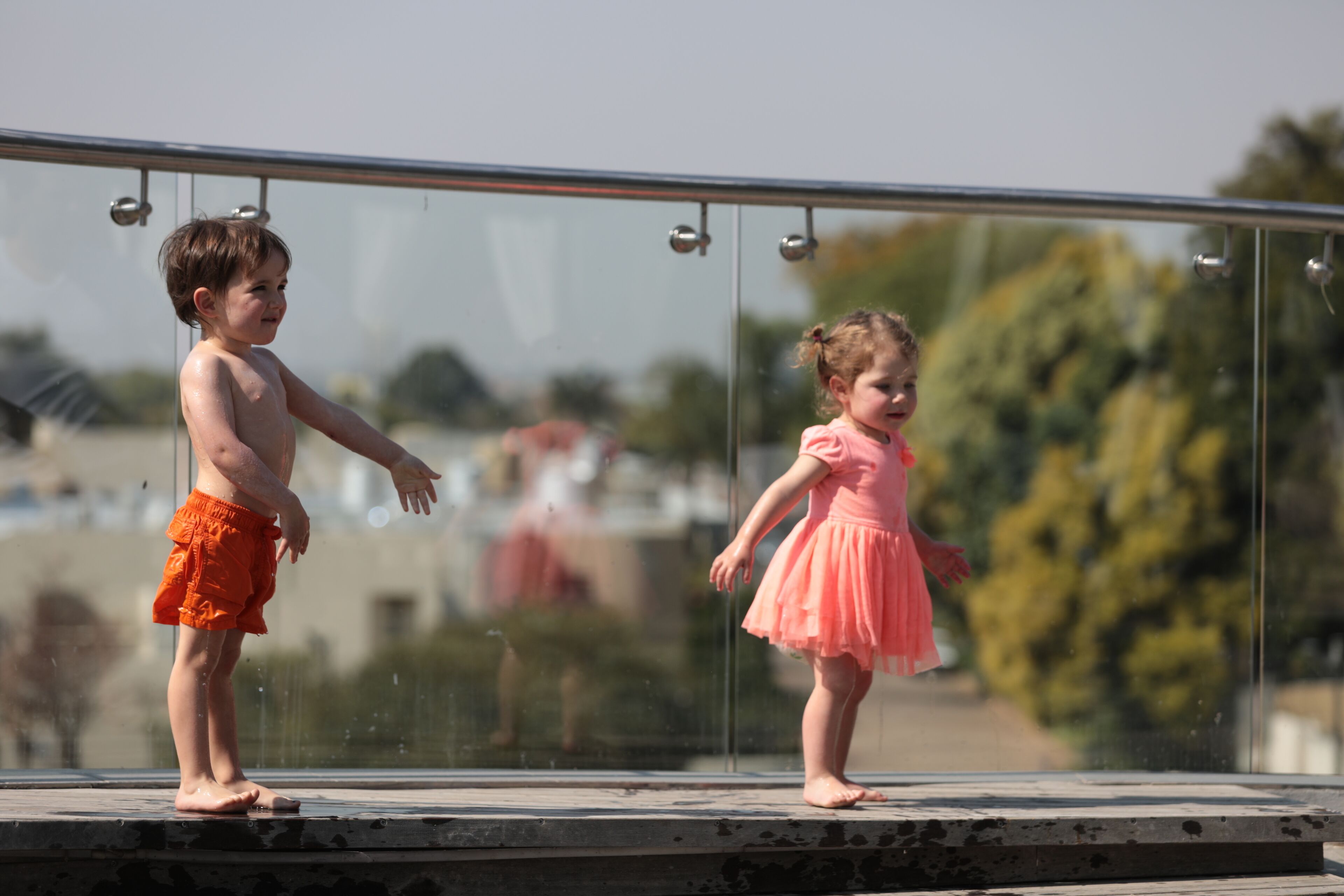 Two children standing on a balcony with a glass railing.