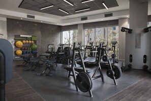 Une salle de sport moderne équipée de divers appareils d’exercice, de stations d’haltérophilie et d’un mur recouvert de ballons médicaux de couleurs vives.