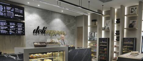 Una cafetería moderna con mostrador de mármol, una vitrina con pasteles y una pizarra de menú.