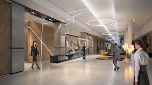 Un hall d’hôtel moderne avec un comptoir d’accueil, un espace d’attente avec des fauteuils et une cuisine visible à l’arrière-plan.