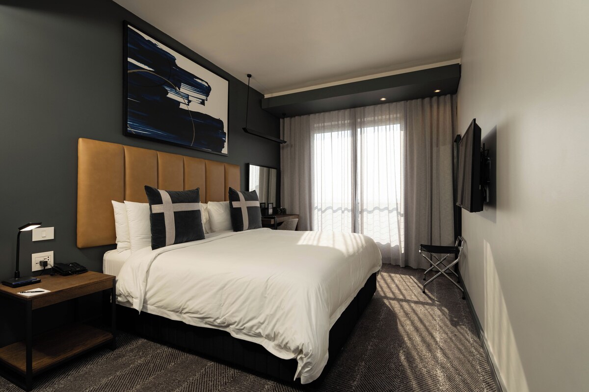 Une chambre d’hôtel avec un grand lit, un bureau avec une lampe, une chaise et un téléviseur fixé au mur.