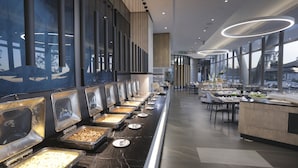 Un buffet avec plusieurs présentoirs de nourriture, un long comptoir et un espace repas avec des tables et des chaises.