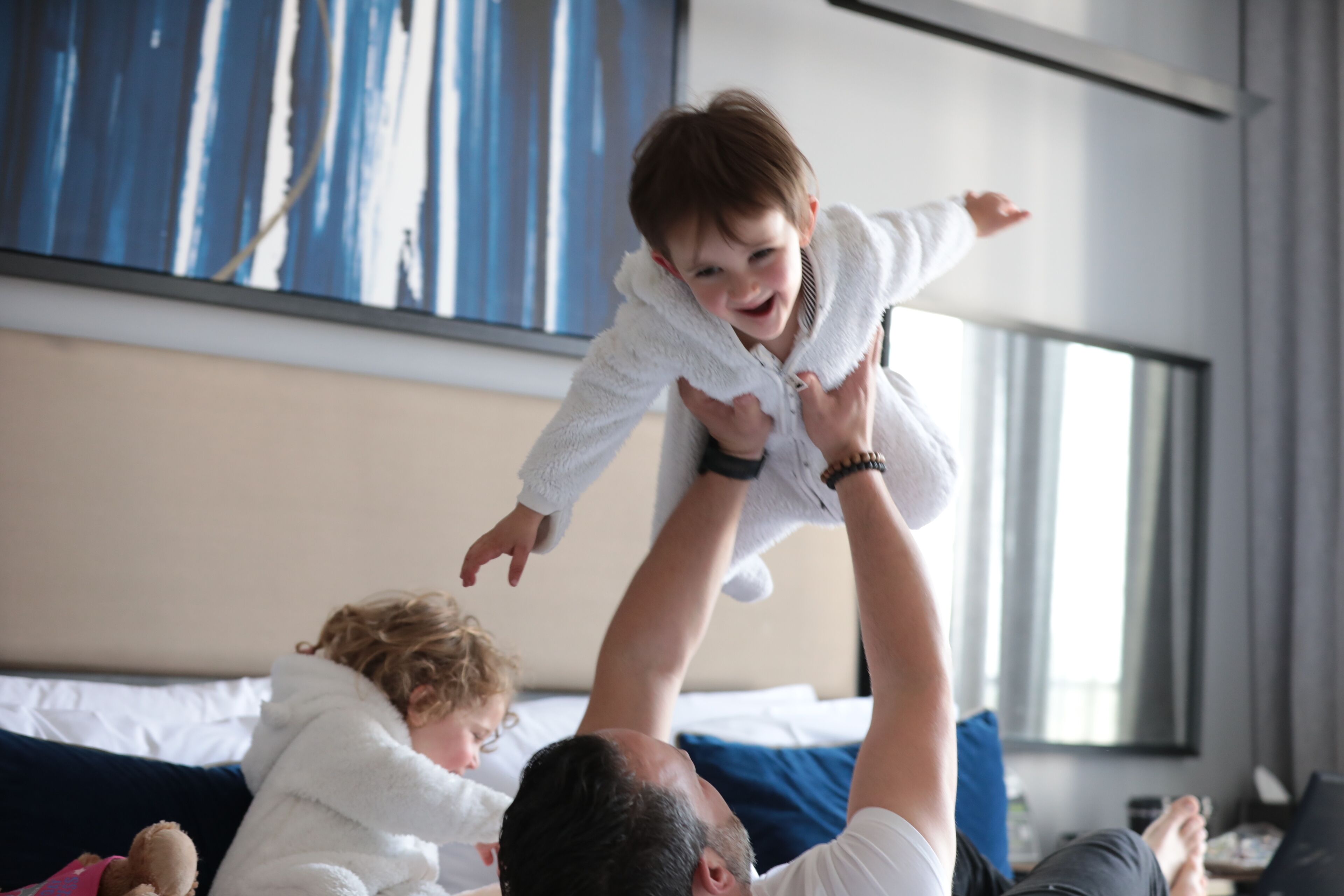 Una familia en una habitación moderna de hotel, con una cama, un ventanal grande y un cuadro en la pared.