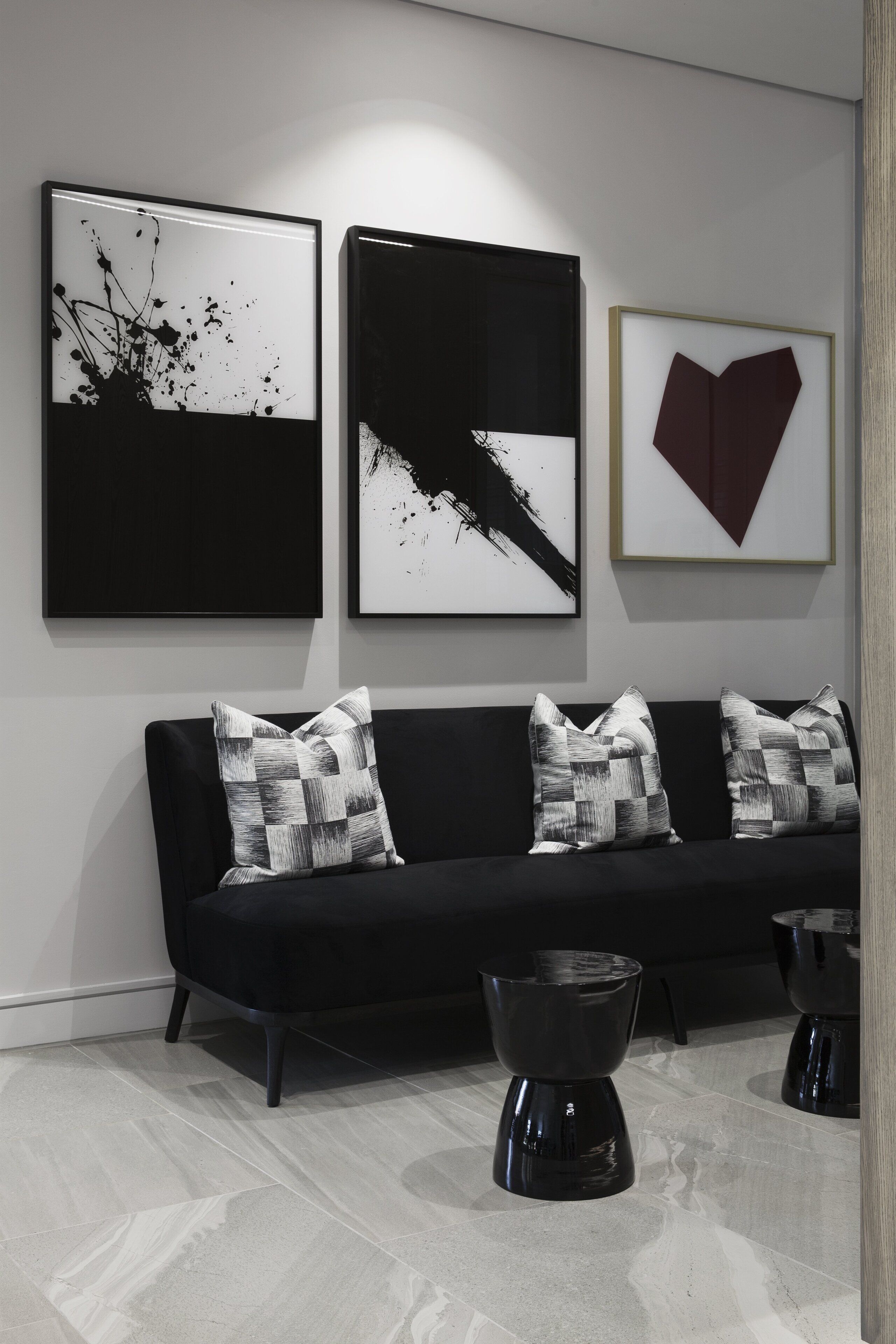 Una sala de estar moderna con un sofá negro, dos mesas de centro negras y tres obras de arte enmarcadas en la pared.