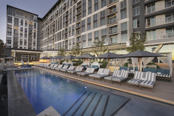 Una piscina al aire libre, sombrillas, sillones reclinables de piscina