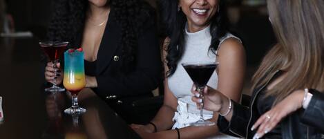 Three people seated at a table with drinks, in a dimly lit indoor setting.